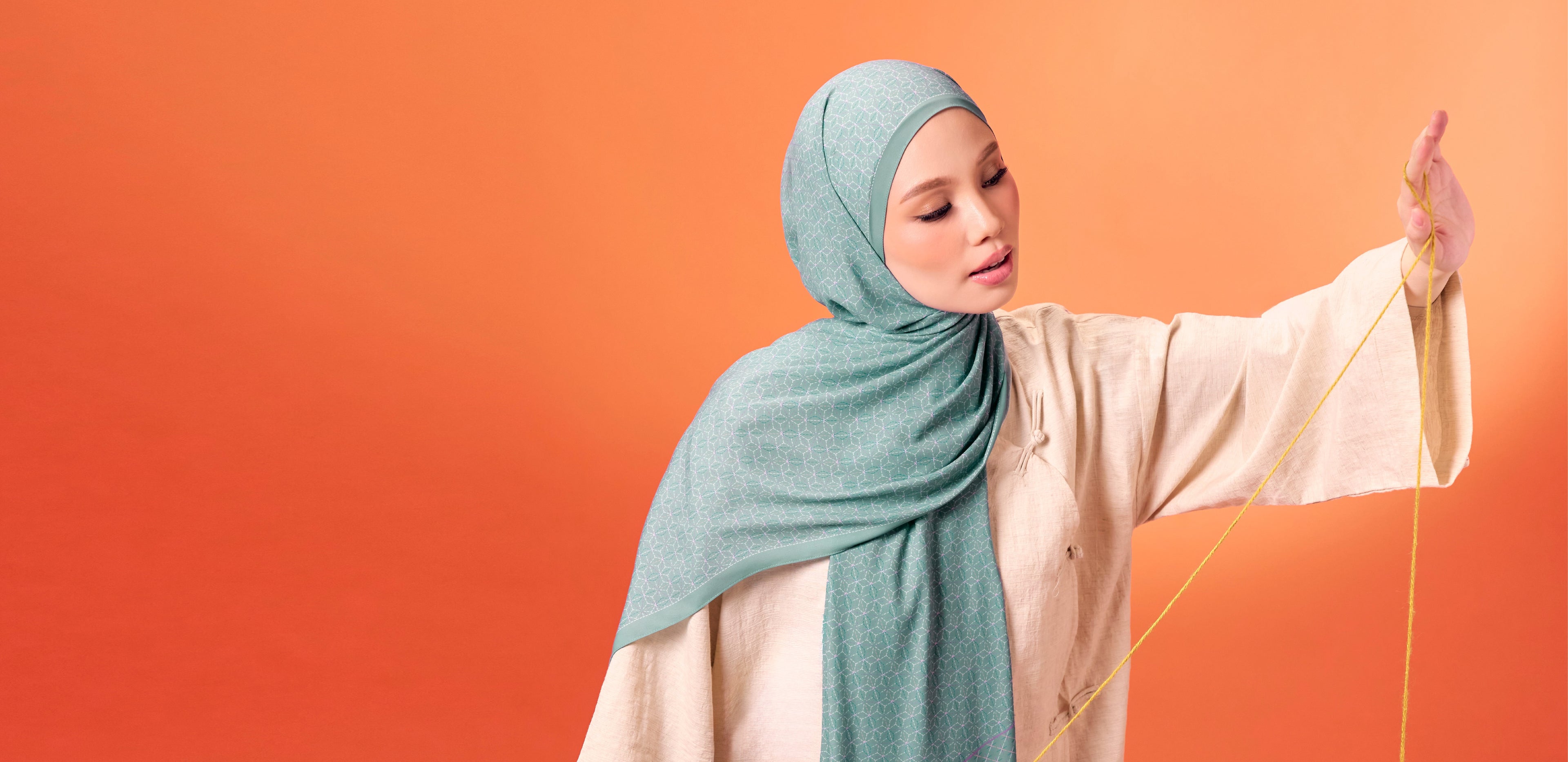 Woman wearing a light blue hijab and beige outfit against an orange background