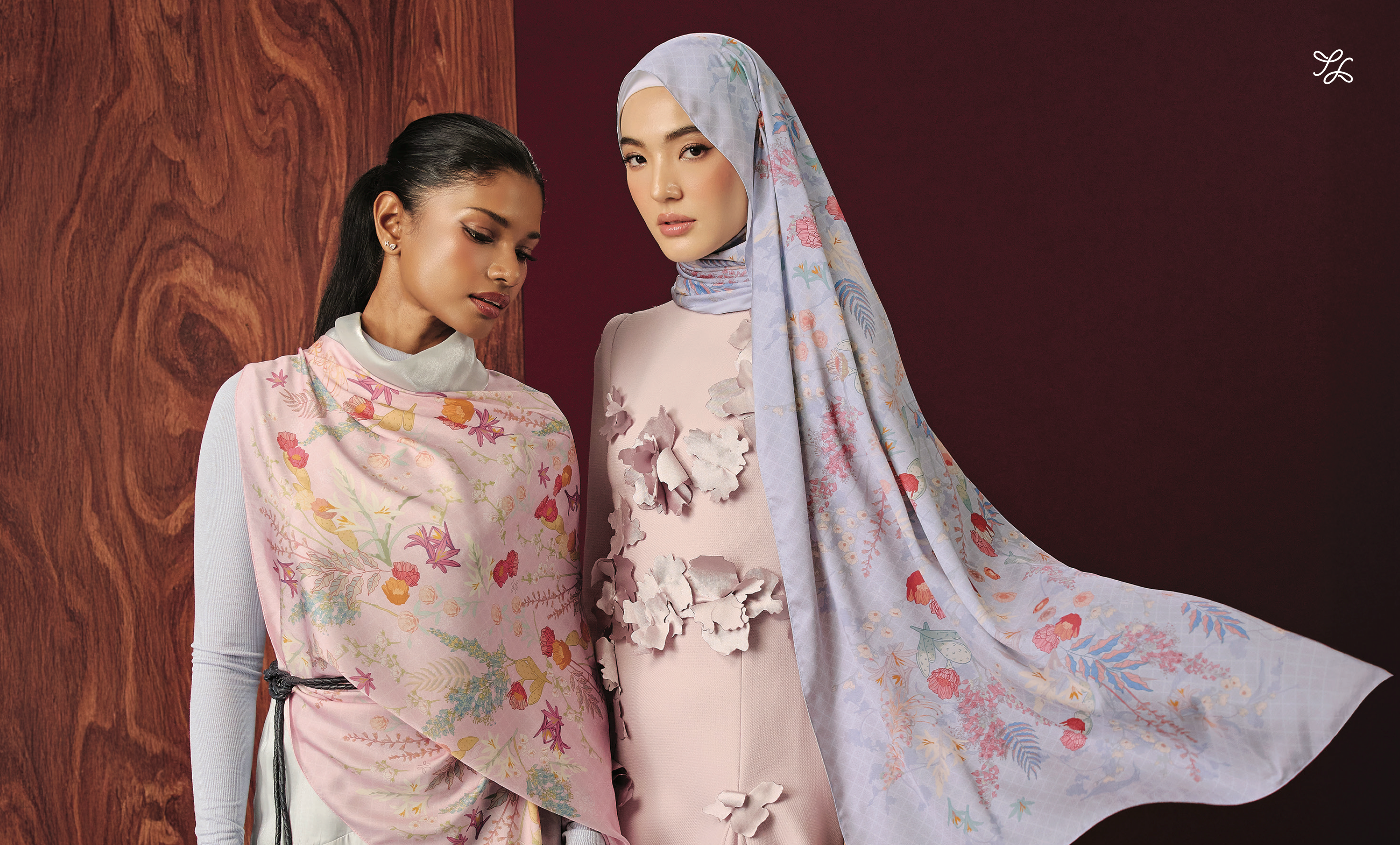 Two women wearing floral hijabs and dresses against a dark background